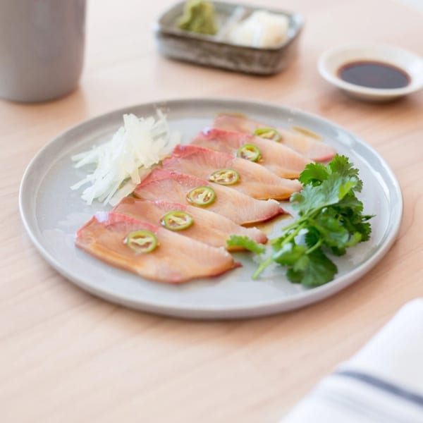 Yume Sushi Bar's yellowtail sashimi with jalapeño, cilantro, and daikon radish on a light plate.
