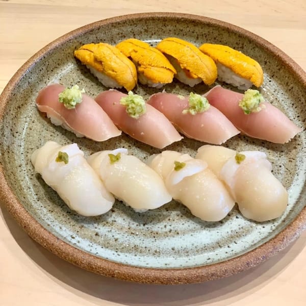 A ceramic plate holds three rows of sushi: uni, tuna, and scallop nigiri, each with a dab of wasabi.