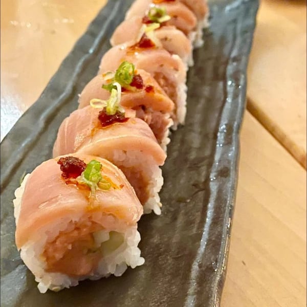 Yume Sushi Bar's sushi roll with salmon, spicy sauce, and green onions on a dark plate.