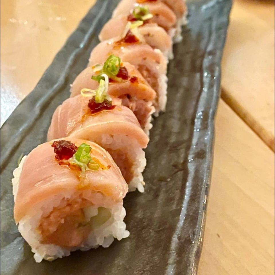 Yume Sushi Bar's sushi roll with salmon, spicy sauce, and green onions on a dark plate.