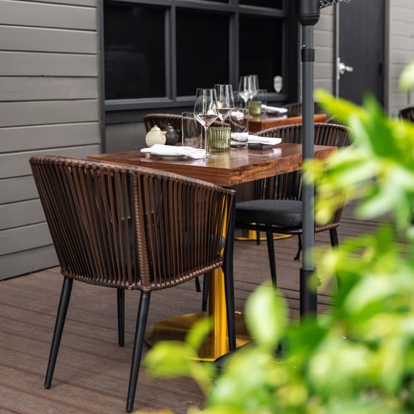 Outdoor dining table at Yume Sushi Bar set with glasses, plates, and teapots, surrounded by chairs.