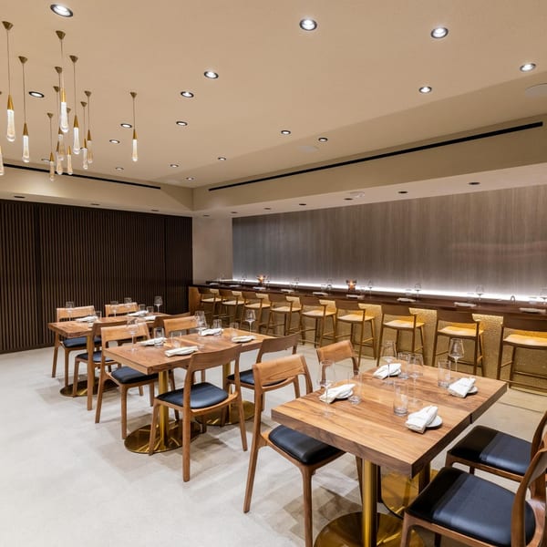 The Yume Sushi Bar dining room with wooden tables, chairs, and a long sushi counter with bar stools.