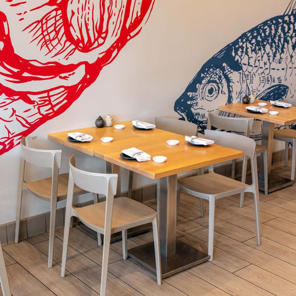 Yume Sushi Bar dining area with light wooden tables, modern chairs, and fish murals on the wall.