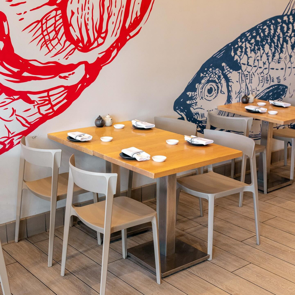 Yume Sushi Bar dining area with light wooden tables, modern chairs, and fish murals on the wall.