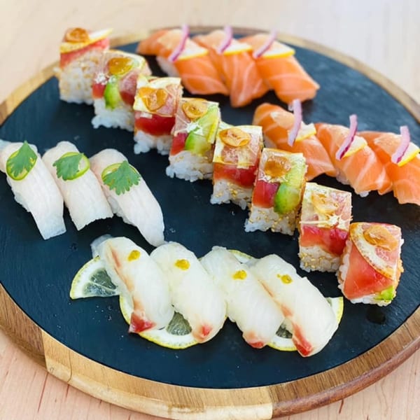 Assorted Yume Sushi Bar sushi rolls and nigiri with salmon, tuna, and white fish on a dark platter.