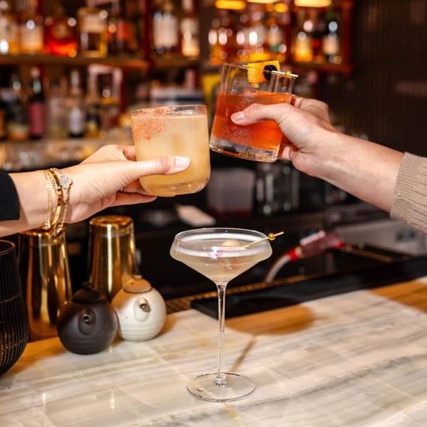 Two people toasting cocktails at Yume Sushi Bar, with a third cocktail on the marble bar.