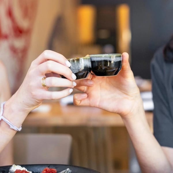 Two people toasting with small, dark ceramic cups at Yume Sushi Bar.