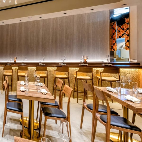 Yume Sushi Bar's elegant dining room with wooden tables, chairs, and a long sushi bar with stools.