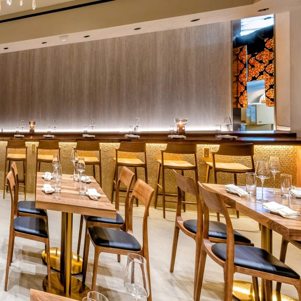 Yume Sushi Bar's elegant dining room with wooden tables, chairs, and a long sushi bar with stools.