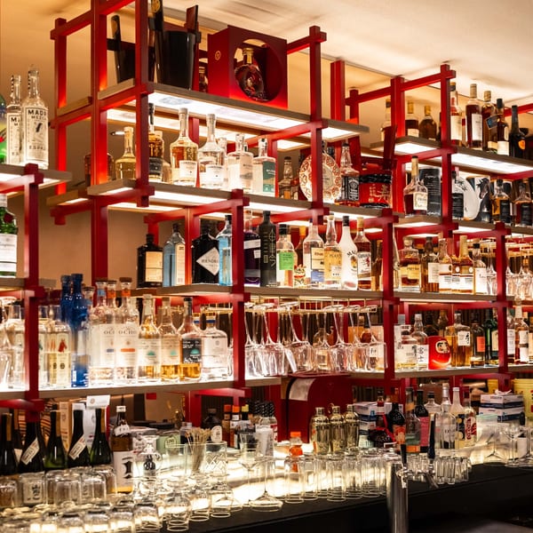 A well-stocked bar at Yume Sushi Bar, featuring red shelves filled with various liquor bottles and glassware.